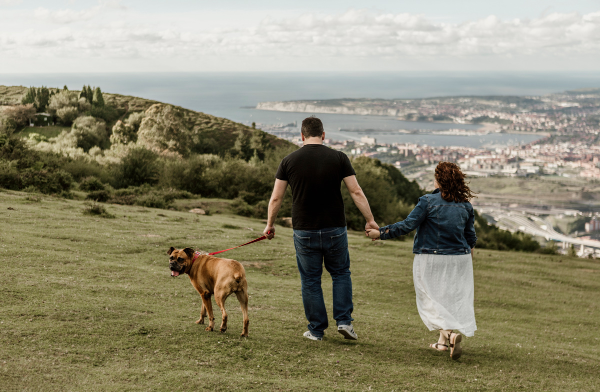 Sesión preboda en Gijón de una pareja caminando con su perro con vistas a la ciudad.
