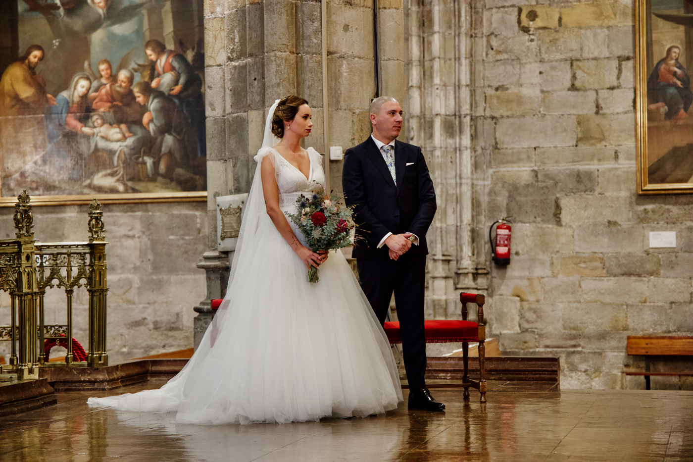 Pareja durante la ceremonia de boda en el interior de una iglesia, con arte religioso y arquitectura clásica de fondo.