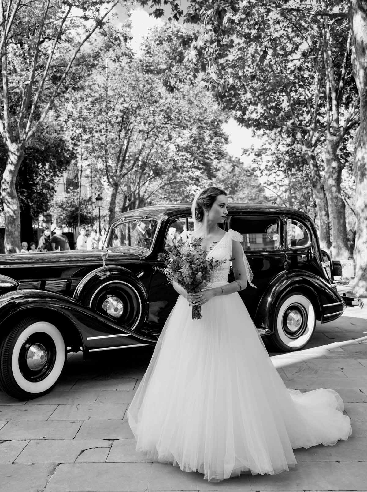 Novia posando con su ramo junto a un coche clásico antes de la ceremonia.