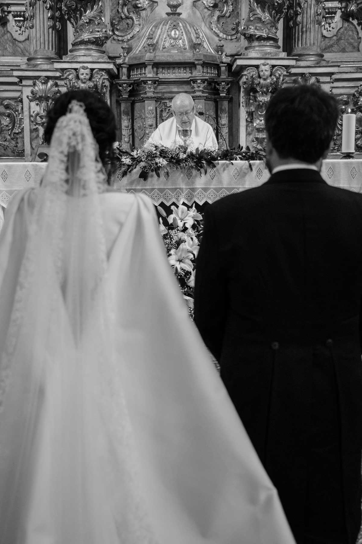 Pareja de novios de espaldas en el altar durante la ceremonia religiosa en una iglesia ornamentada.