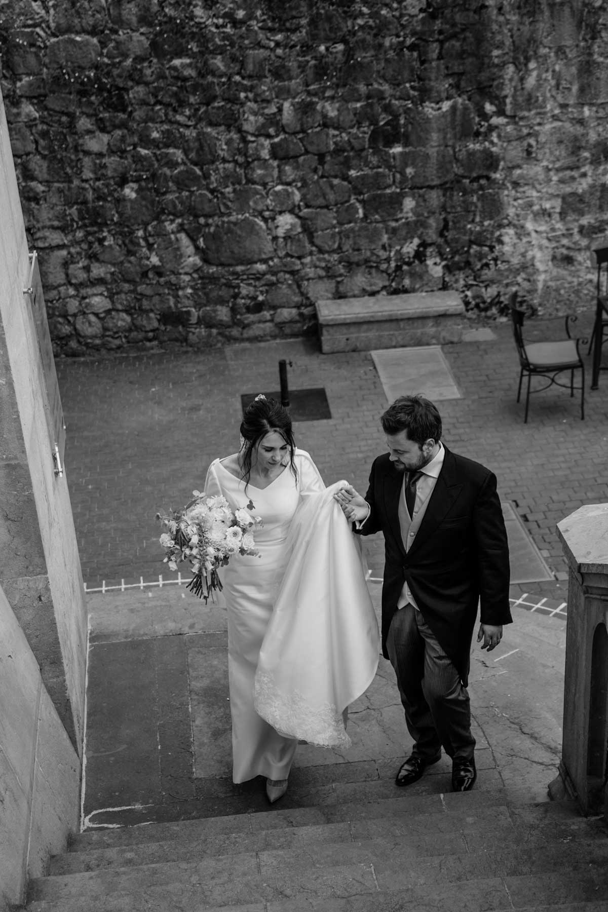 Pareja de recién casados subiendo unas escaleras en un exterior de piedra después de la ceremonia.