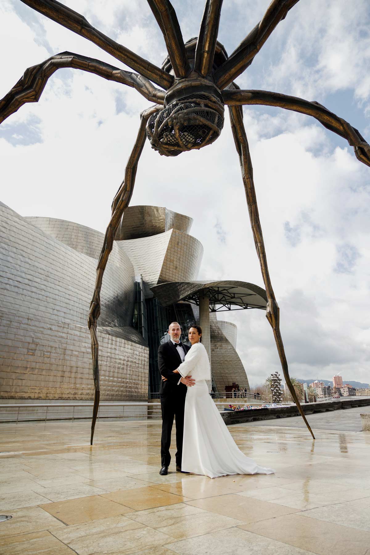 Pareja de novios posando bajo la escultura Maman junto al Museo Guggenheim de Bilbao — fotografía artística y moderna de North Producciones