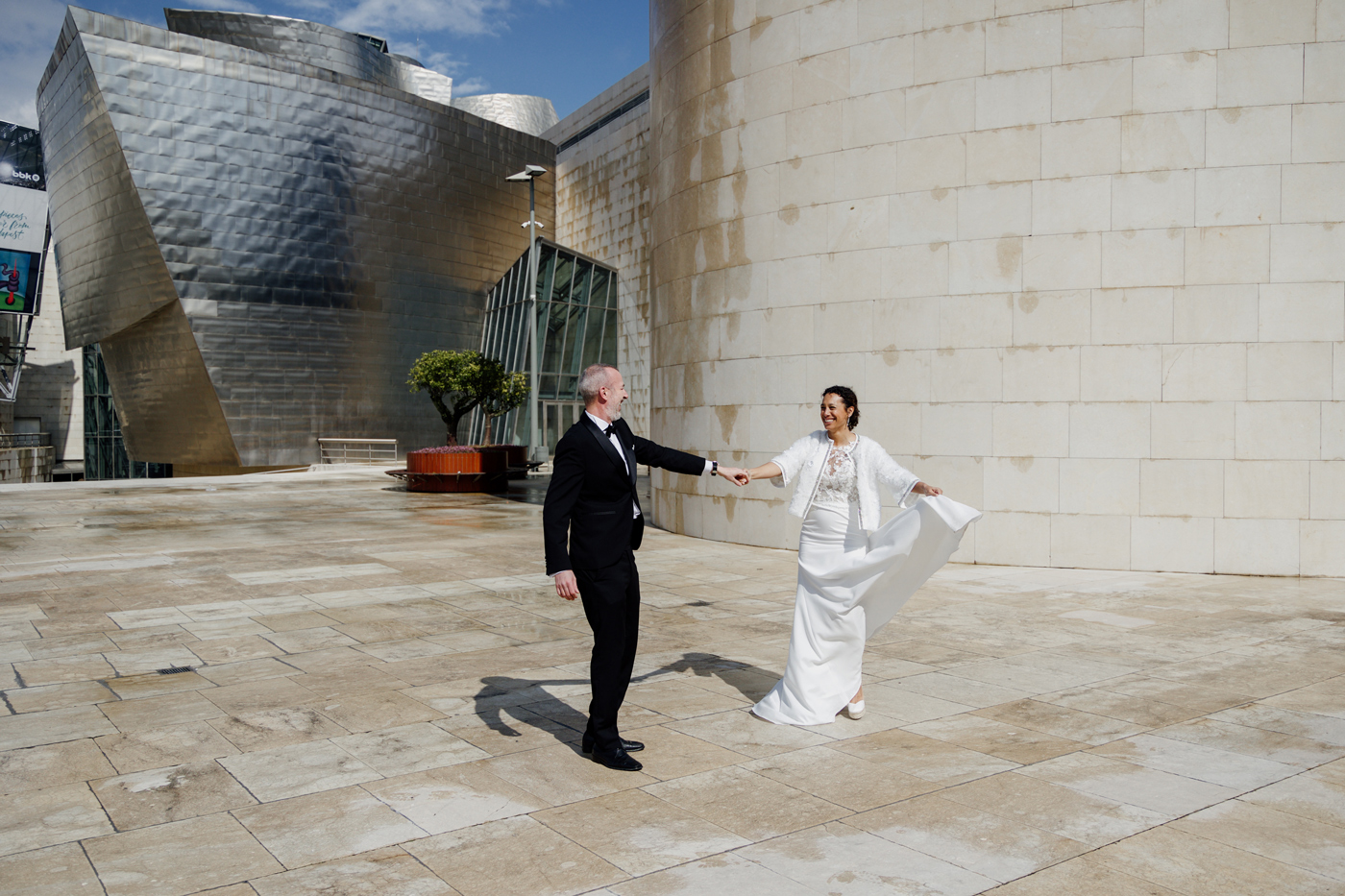 Pareja de novios caminando juntos frente al Museo Guggenheim Bilbao durante su boda, fotografía realizada por un fotógrafo de bodas en Bilbao.