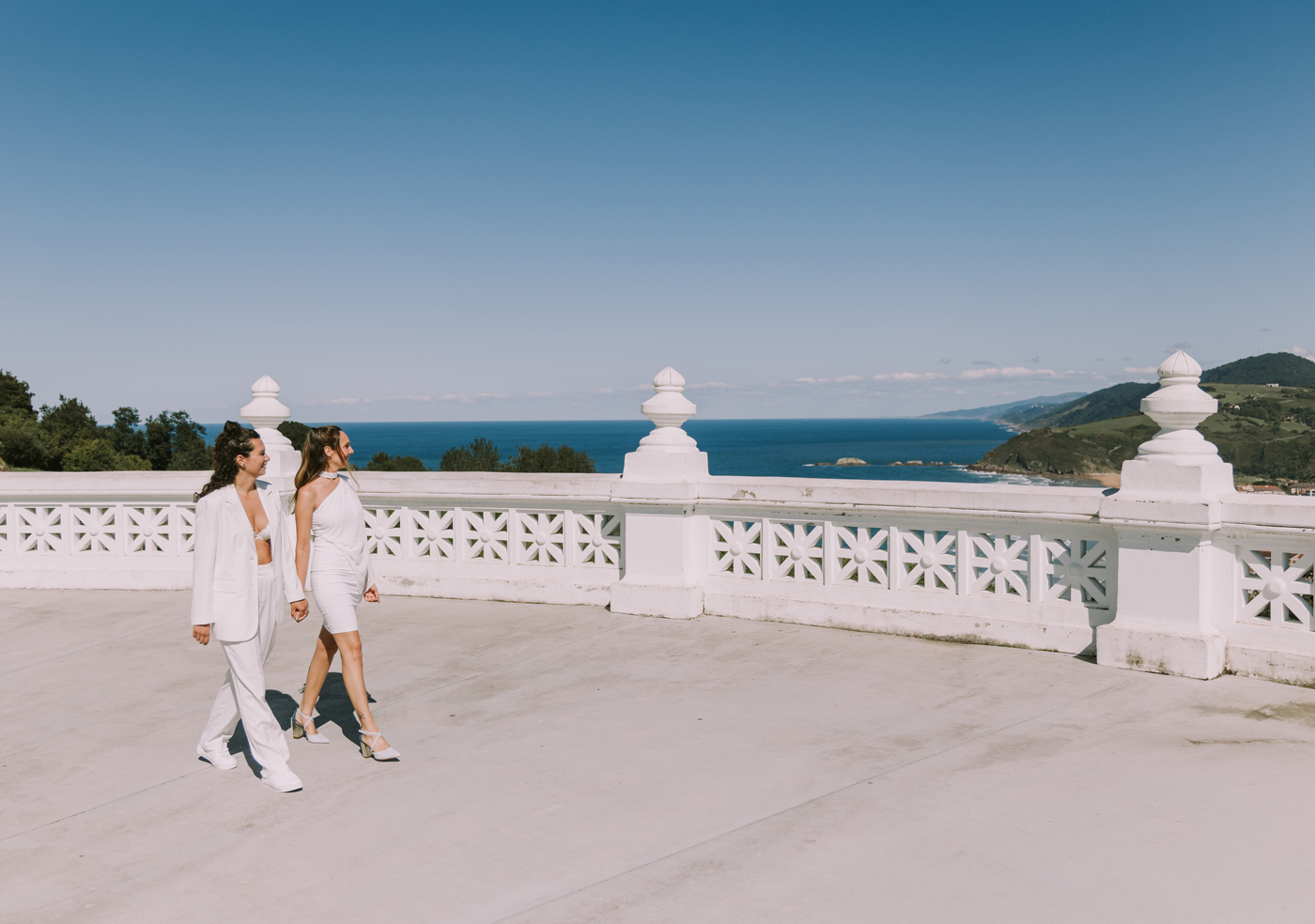 Pareja de novias caminando de la mano en el mirador de Vista Alegre en Zarautz, con el mar Cantábrico de fondo, fotografiadas por un fotógrafo de bodas en Bilbao y Bizkaia.