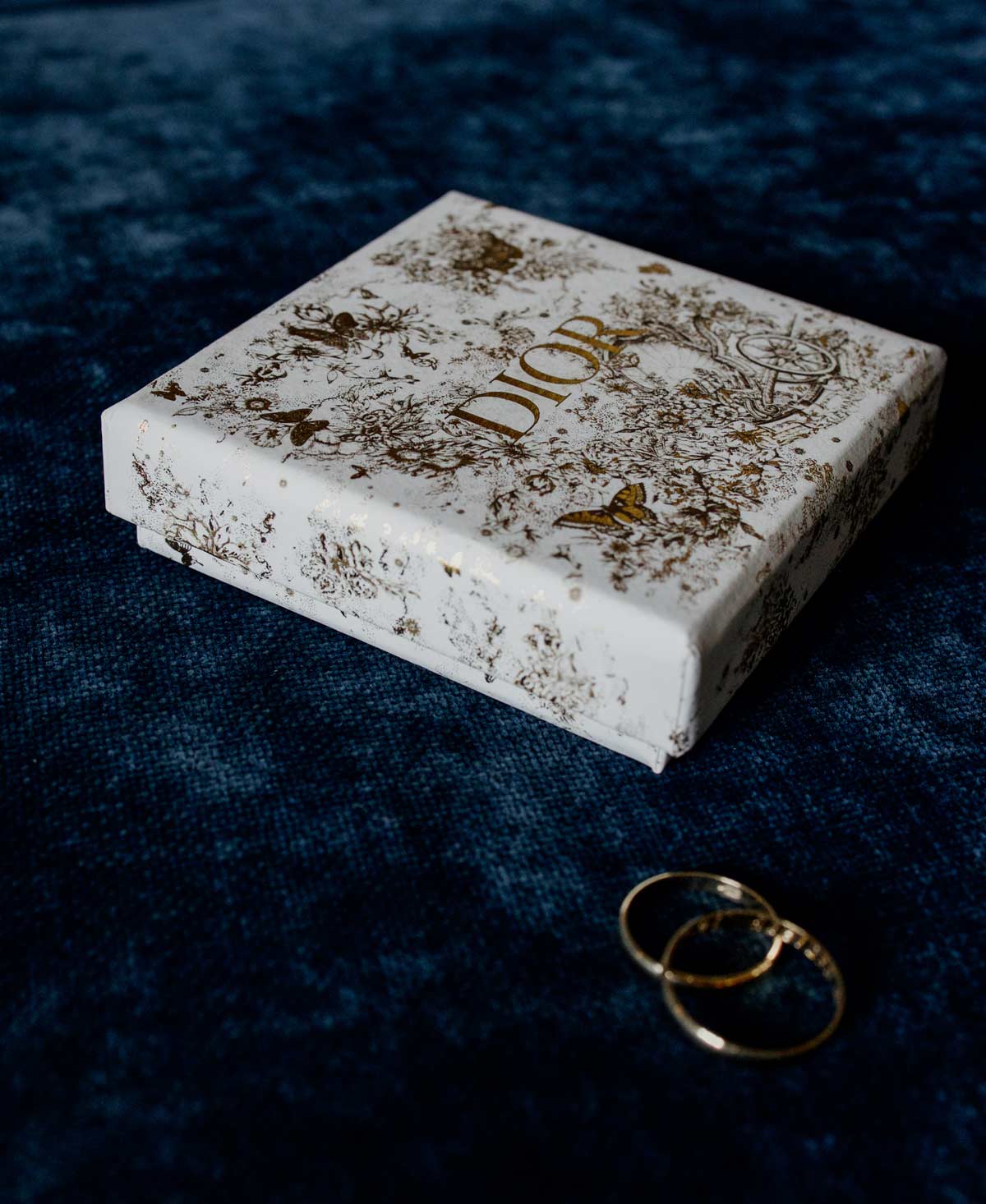 Fotografía de los anillos de boda junto a una caja decorativa de Dior sobre fondo azul, capturada por un fotógrafo de bodas en Bizkaia.