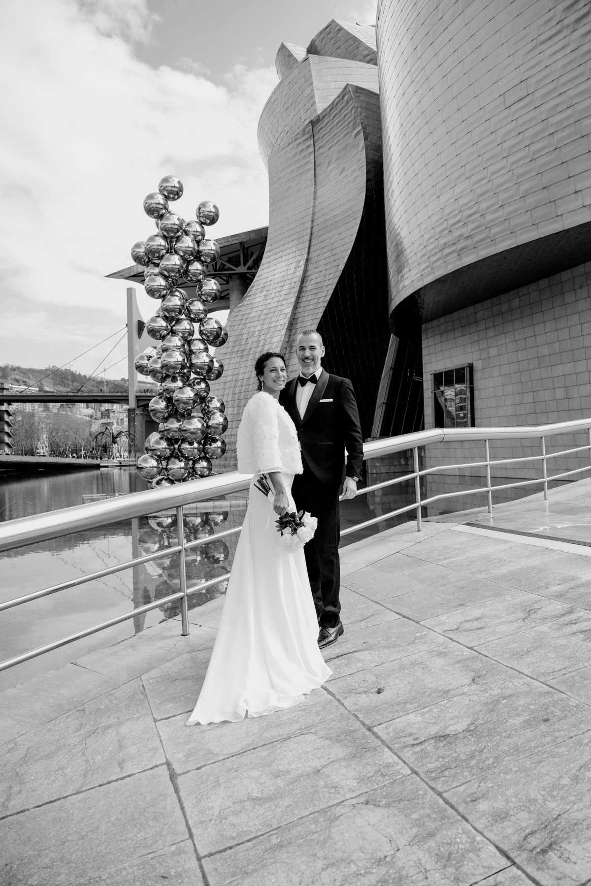 Novios posando frente al Museo Guggenheim Bilbao en una fotografía de boda en blanco y negro realizada por un fotógrafo de bodas en Bilbao.