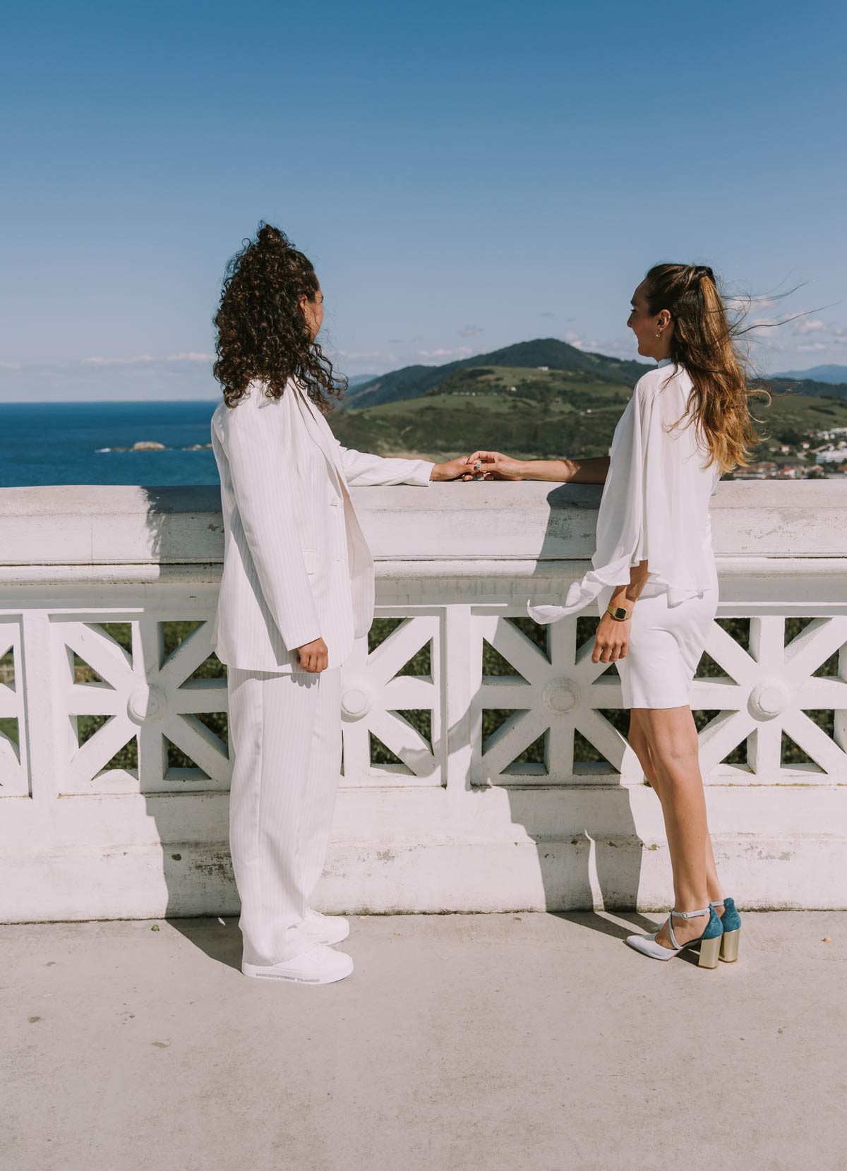 Pareja de novias vestidas de blanco posando frente al mar en una sesión de boda, fotografía realizada por un fotógrafo de bodas en Bilbao y Bizkaia.