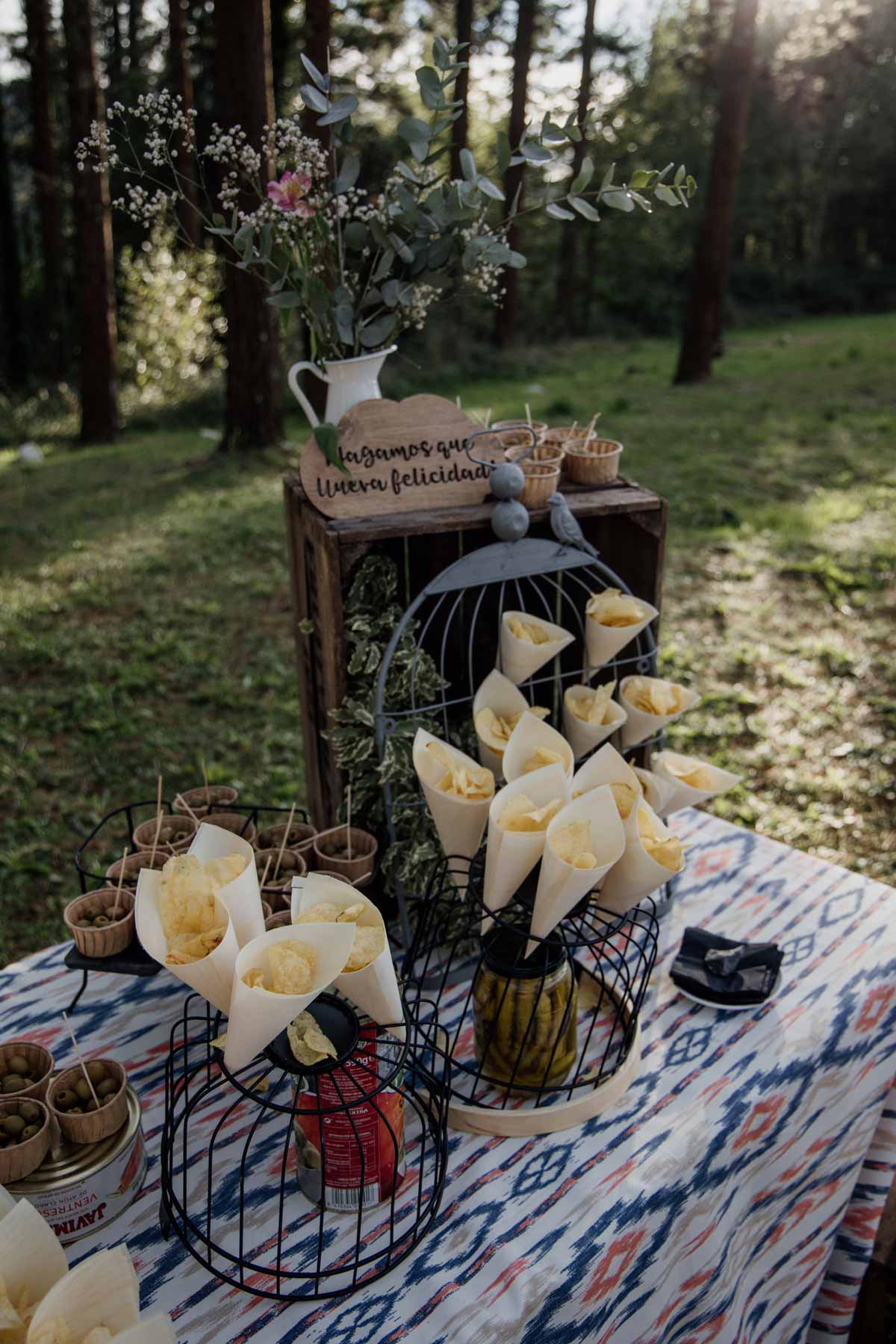 "Mesa decorativa con conos de pétalos, flores y detalles rústicos en una boda al aire libre en Bilbao."