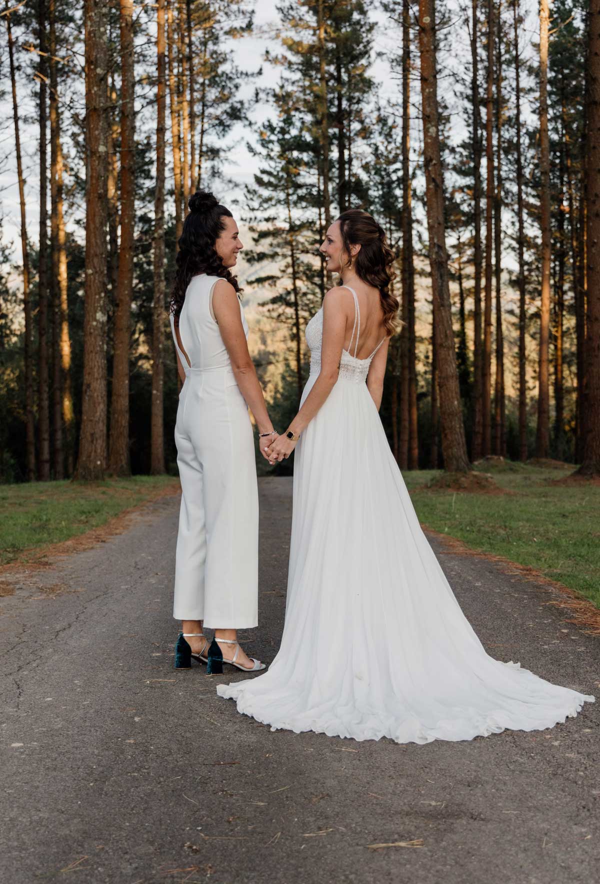 "Dos novias caminando de la mano por un camino rodeado de árboles durante su boda en Bizkaia."
