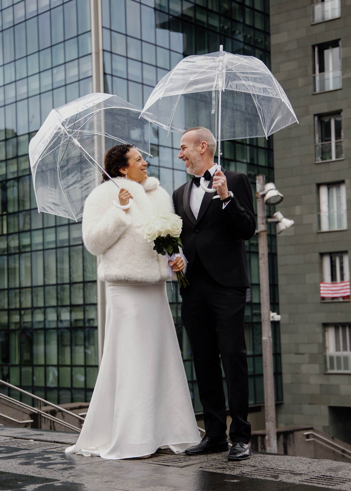 Pareja de recién casados posando bajo la lluvia con paraguas trasparentes en Bilbao