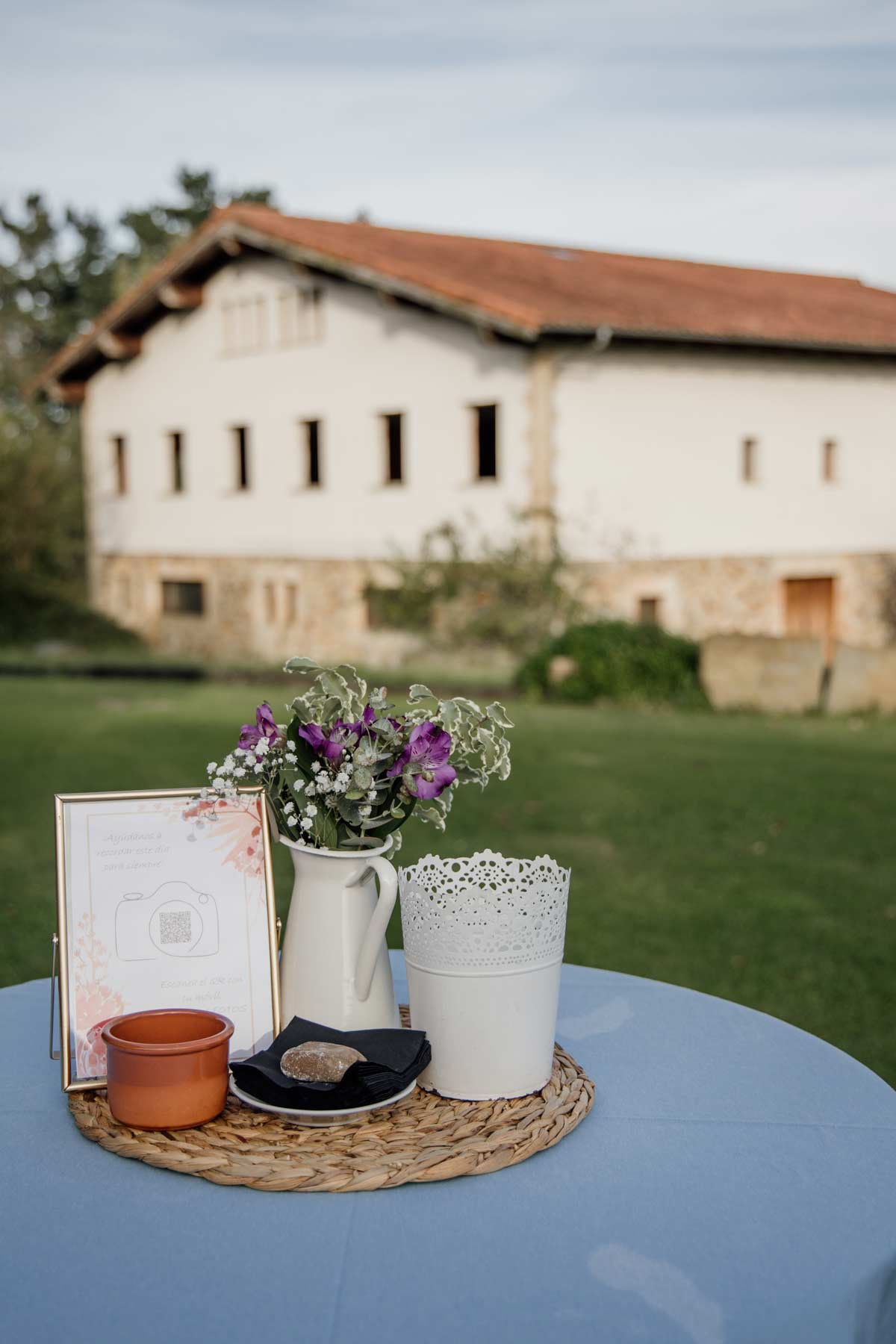"Mesa decorativa de boda con flores y cartel frente a un caserio vasco, fotografía de detalles de boda en Euskadi."