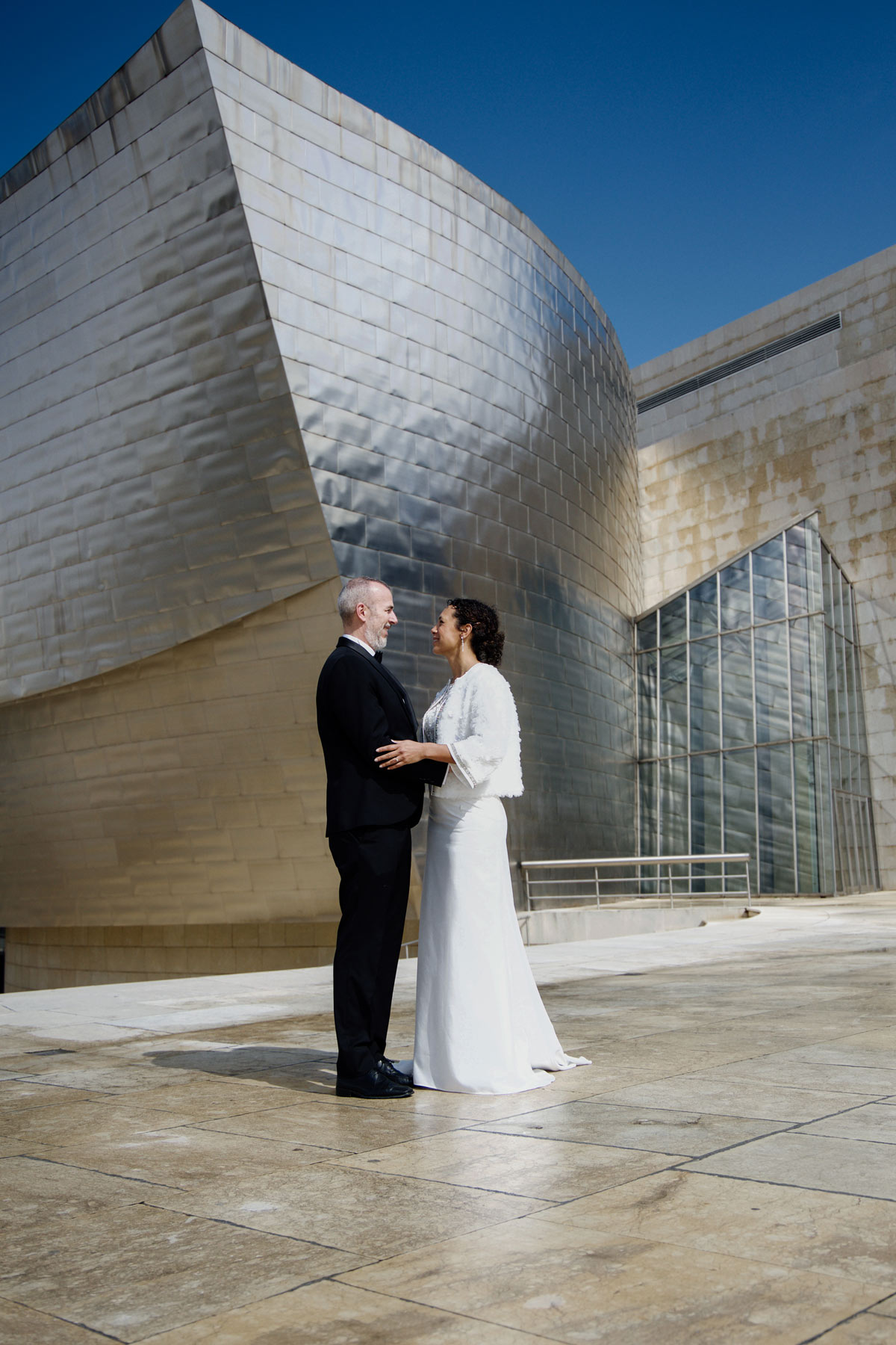 Novios posando frente a la arquitectura metálica del Museo Guggenheim Bilbao en una fotografía realizada por un fotógrafo de bodas en Bilbao.