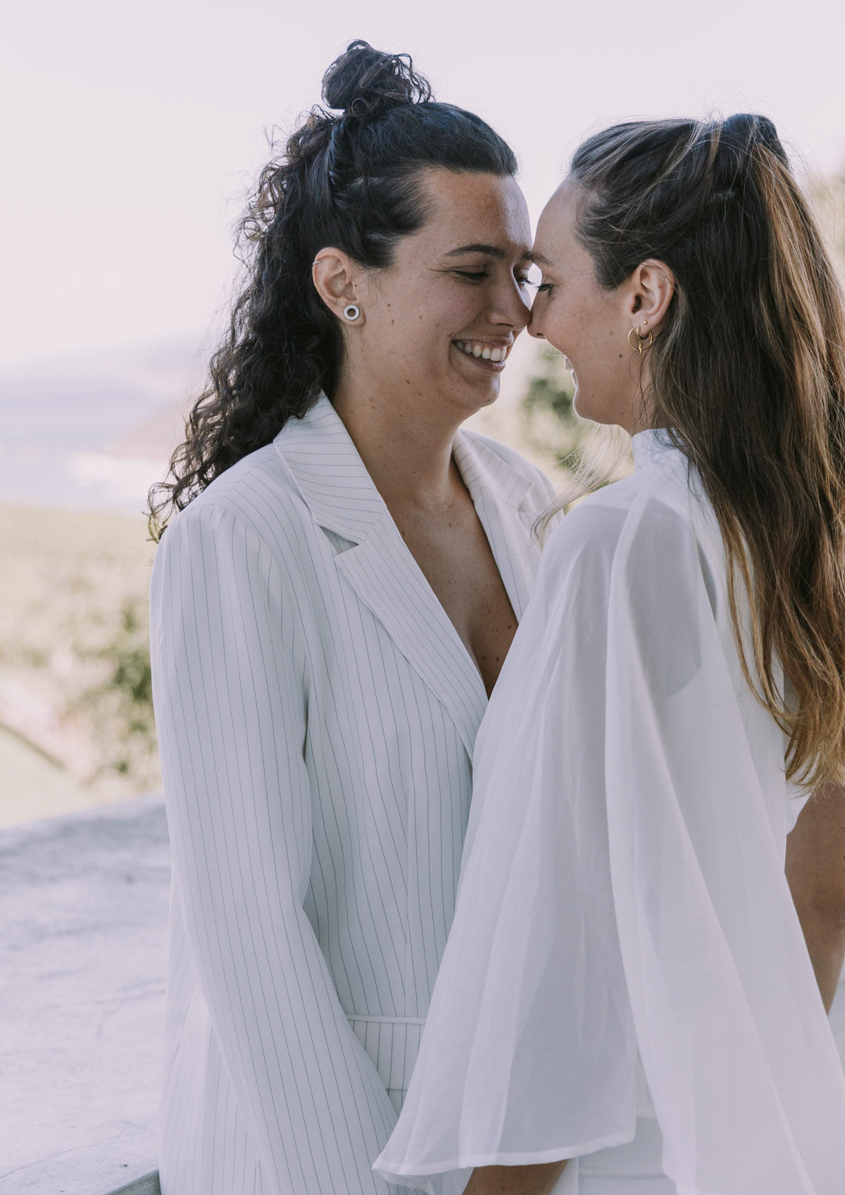 Pareja de novias sonriendo juntas durante su sesión de boda al aire libre, fotografía natural y emotiva.