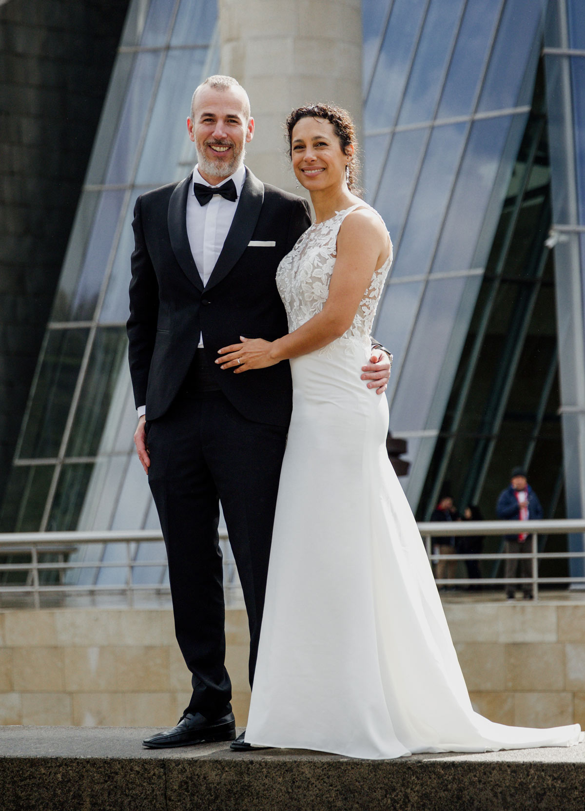 Pareja de novios posando juntos frente a un edificio moderno en un reportaje realizado por fotógrafos de bodas en Bizkaia.