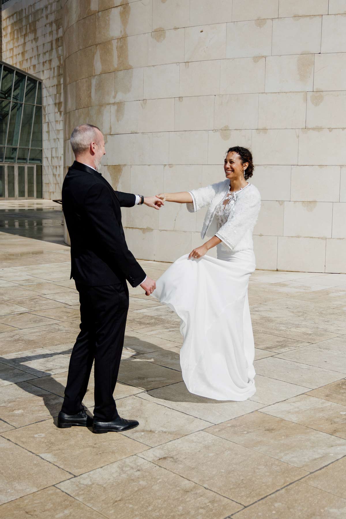 Pareja de novios bailando frente a una fachada moderna en un reportaje capturado por un fotógrafo de bodas en Bilbao.