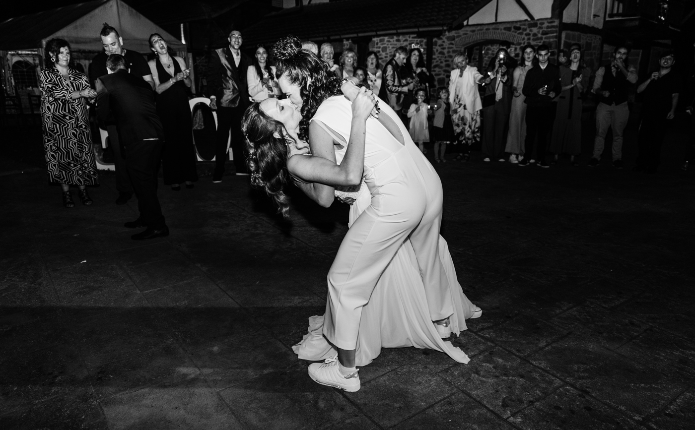 Pareja bailando durante la celebración de una boda, capturada en blanco y negro con invitados alrededor
