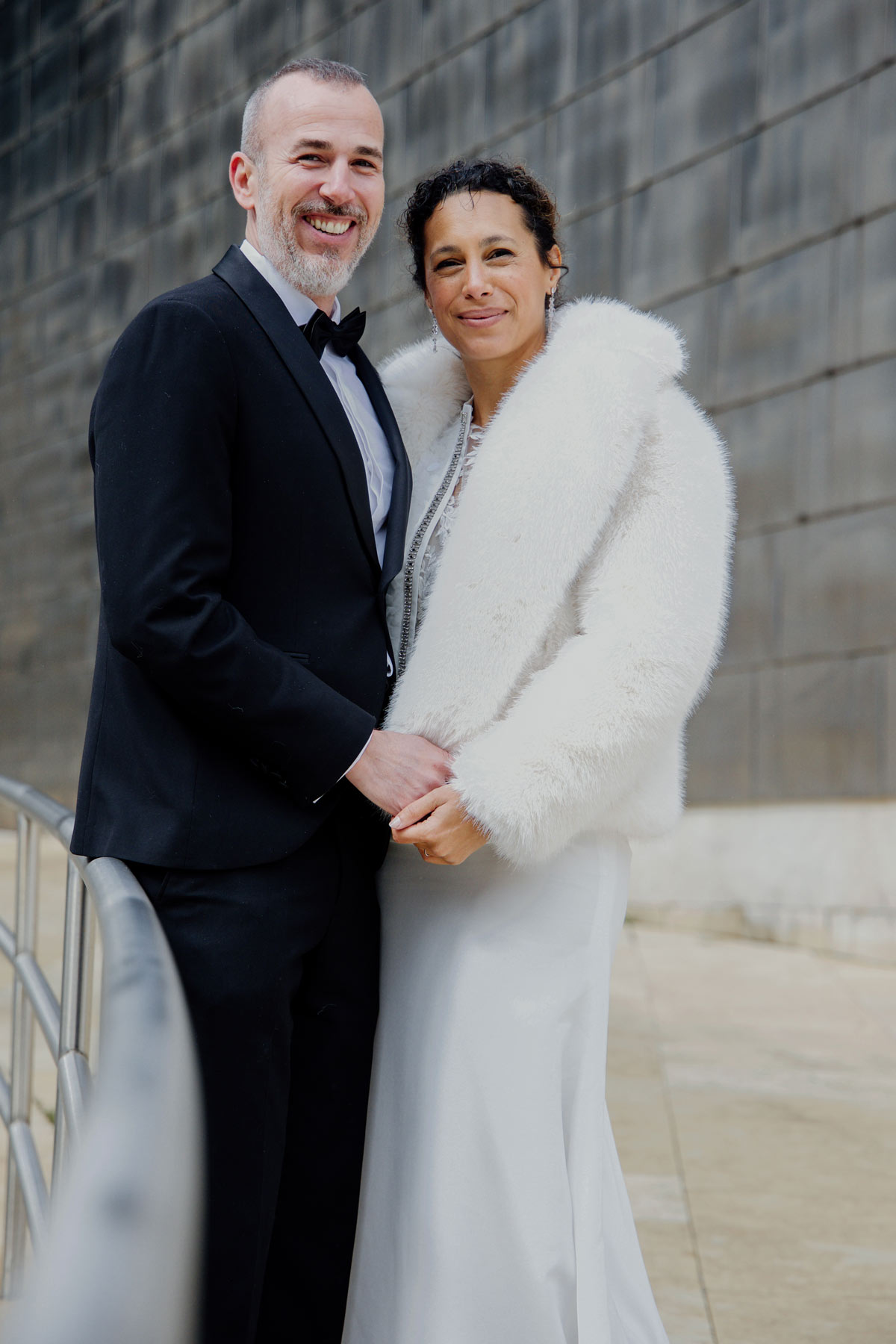 Pareja de boda posando al aire libre junto a una pared de piedra en Bilbao, en un reportaje fotográfico natural y elegante.