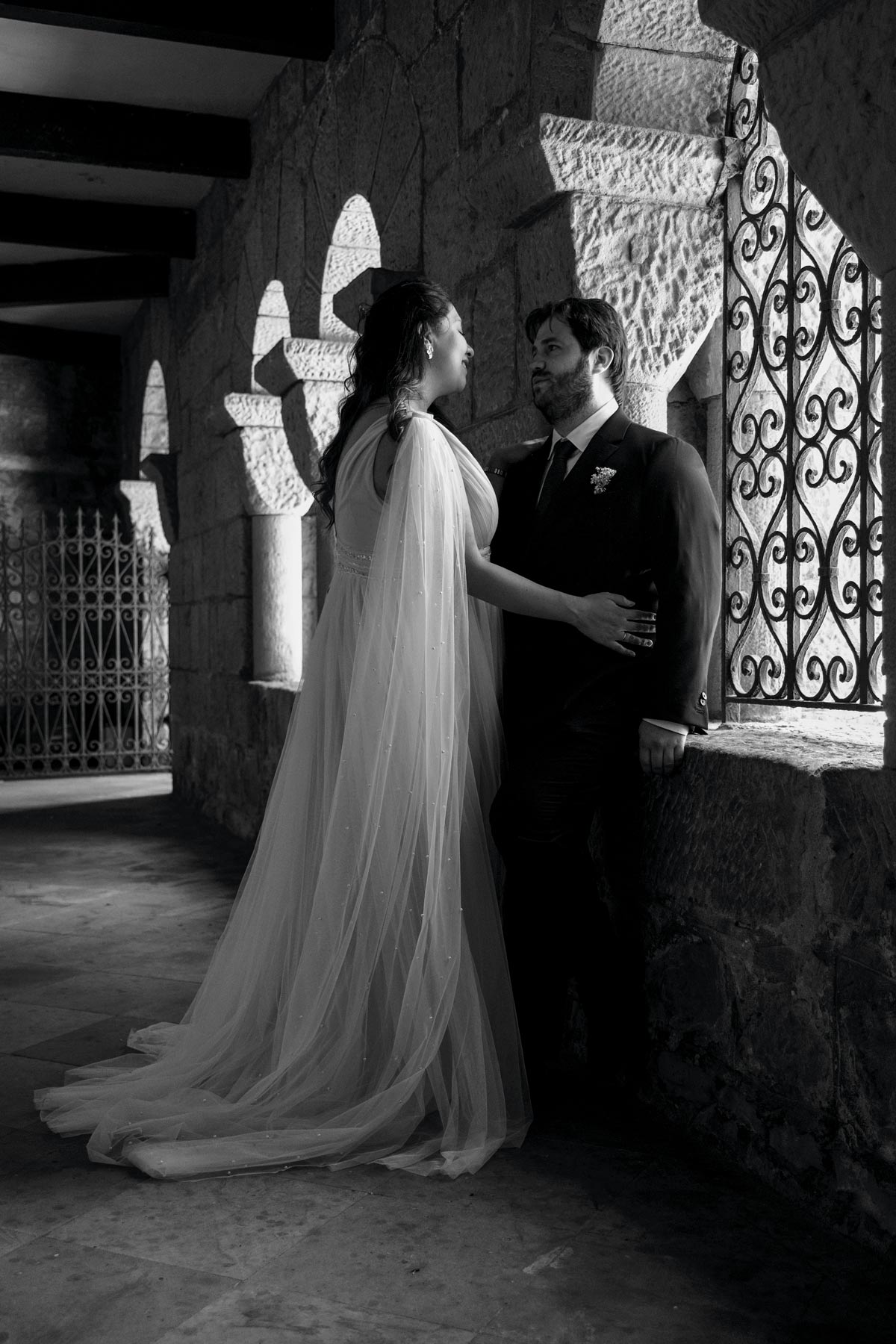 Pareja de novios posando en un pasaje de piedra iluminado por arcos durante su boda en Bilbao — fotografía artística en blanco y negro de North Producciones