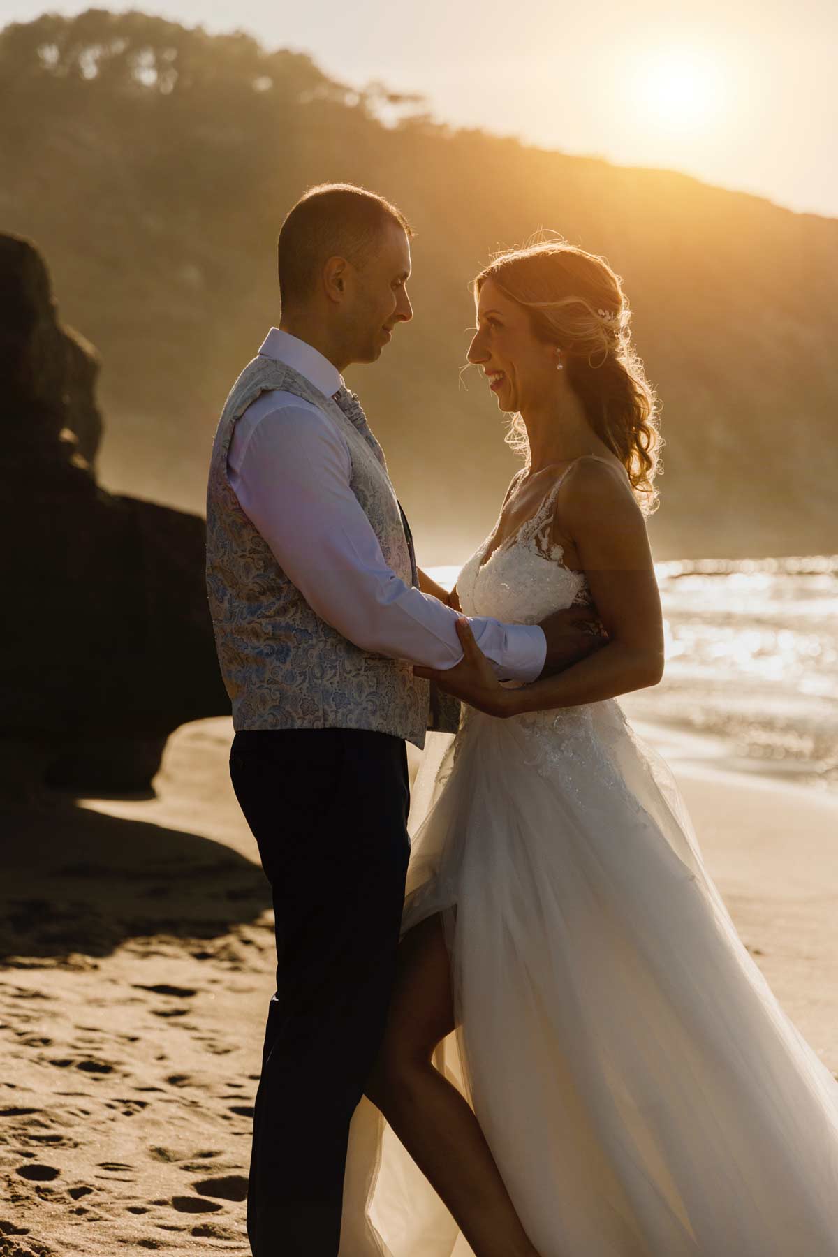 Pareja de recién casados abrazándose en la playa al atardecer durante su sesión de postboda en Bilbao — fotografía luminosa y natural de North Producciones