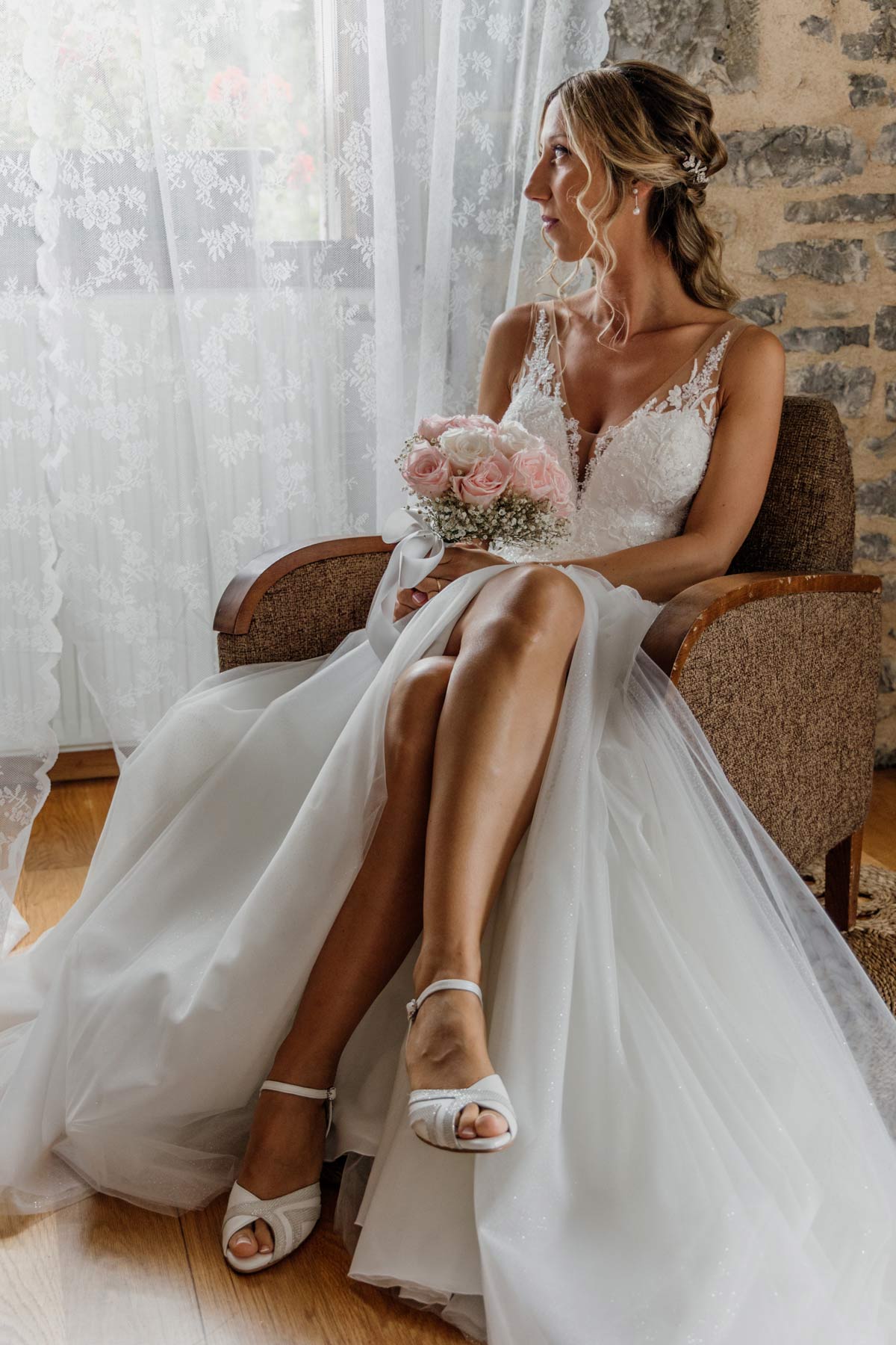 Novia sentada en un sillón mirando hacia la ventana mientras sostiene su ramo durante su boda en Bilbao — fotografía elegante y natural de North Producciones