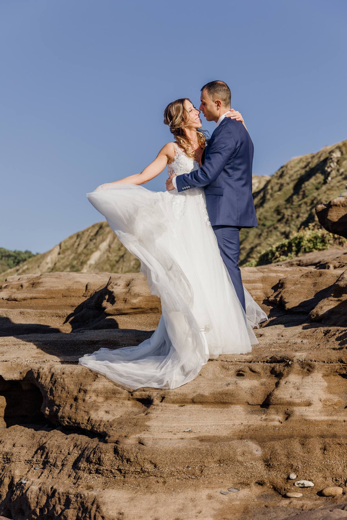 Pareja de recién casados abrazándose sobre formaciones rocosas durante su boda en Cantabria — fotografía natural y luminosa de North Producciones