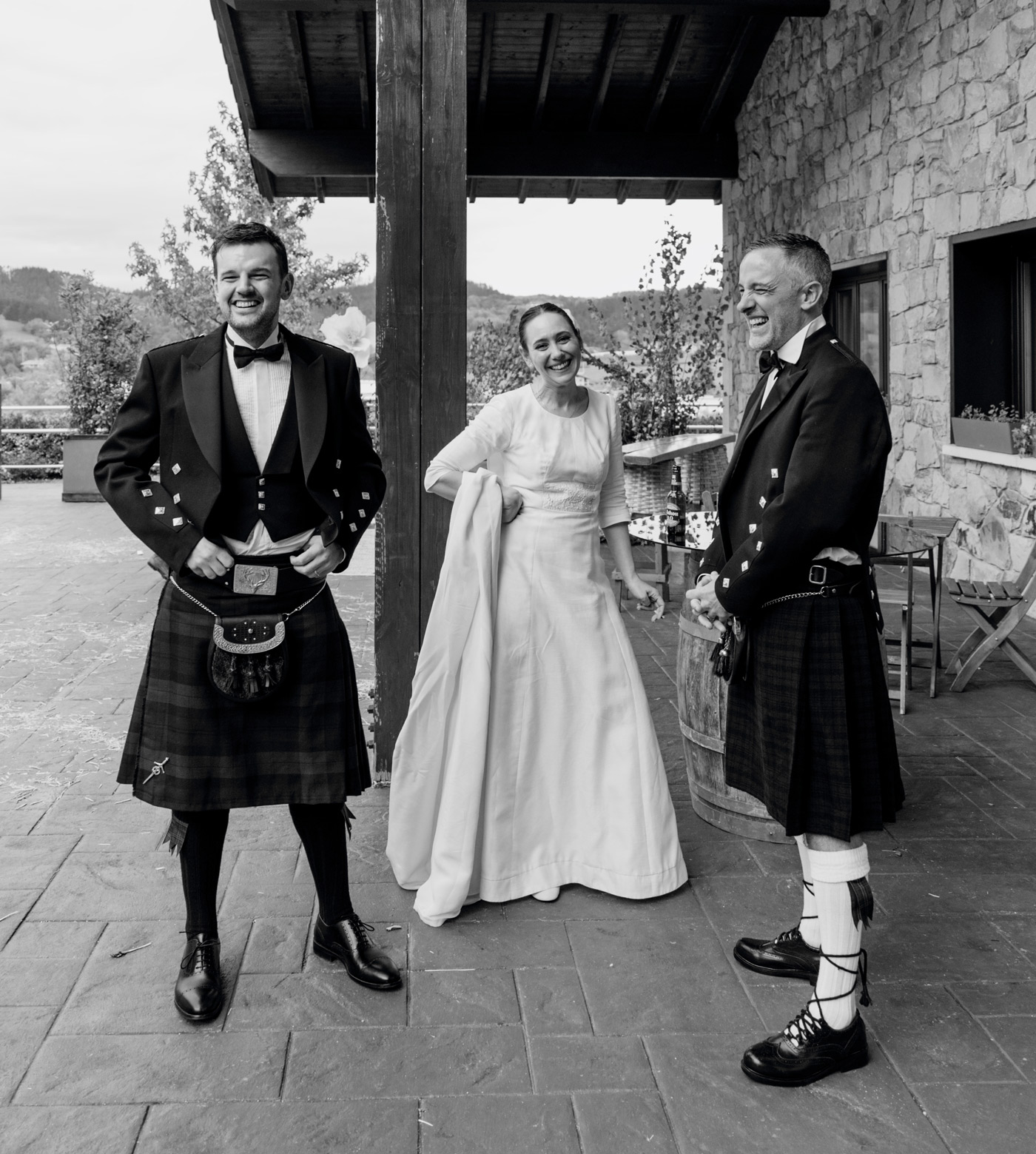 Novia conversando y riendo con dos invitados en traje tradicional durante una boda en Santander — fotografía documental en blanco y negro de North Producciones