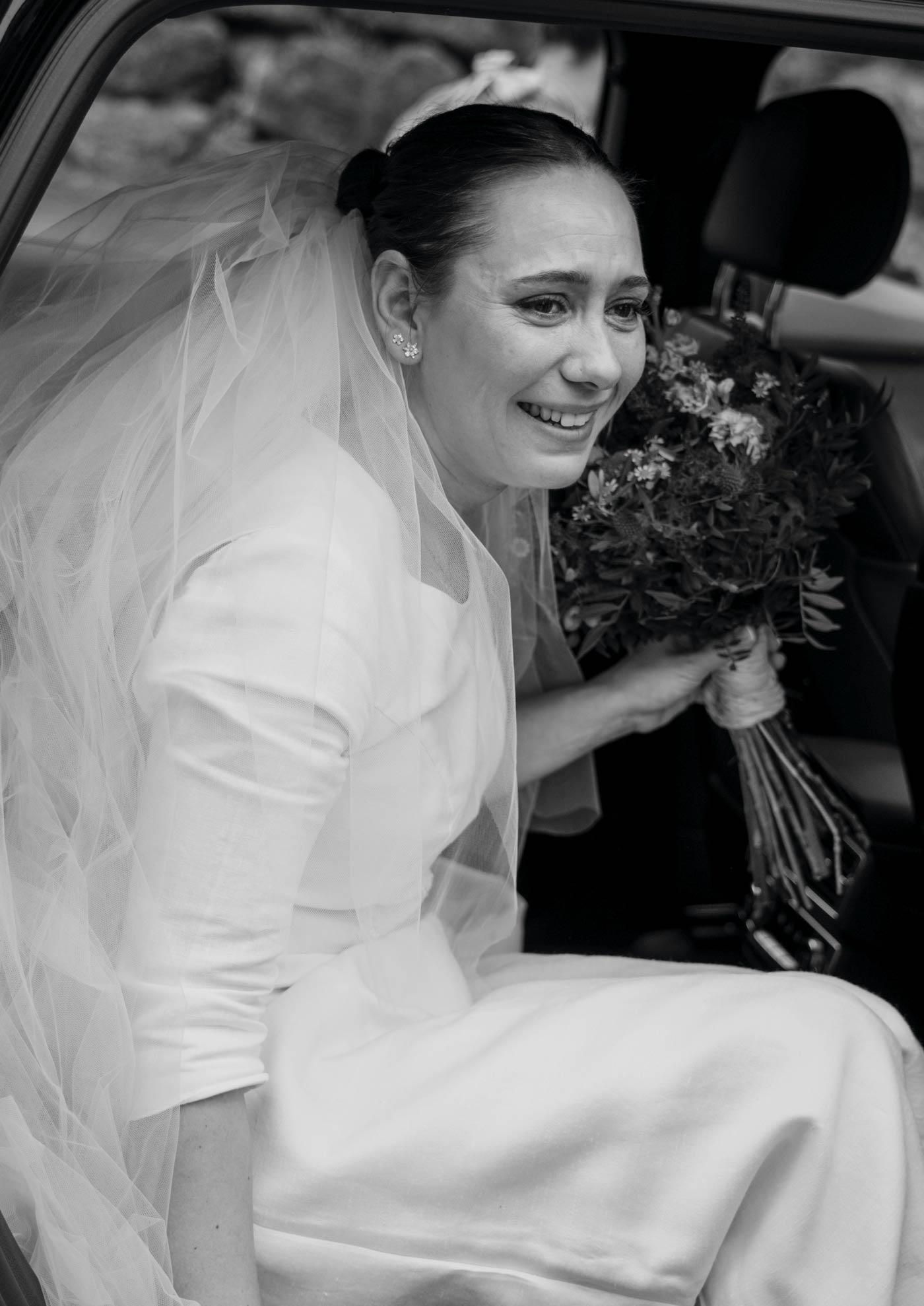 Novia saliendo del coche con su ramo el día de su boda en Bilbao — fotografía emocional en blanco y negro de North Producciones