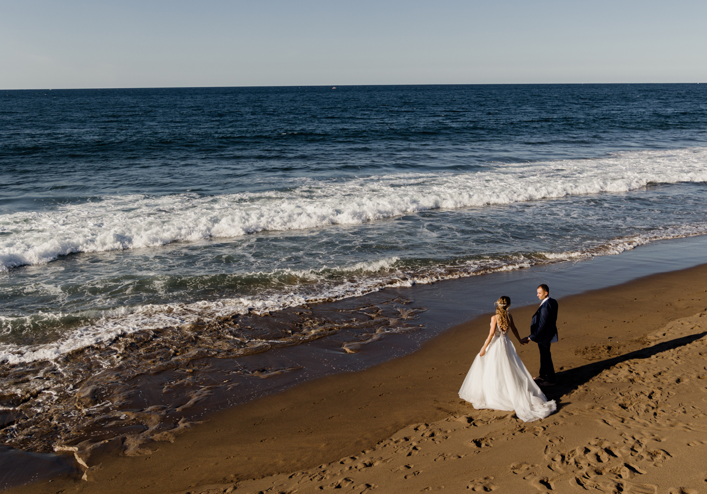 Pareja de recién casados caminando por la orilla del mar durante su sesión de postboda en la playa de Bizkaia — fotografía natural y luminosa de North Producciones
