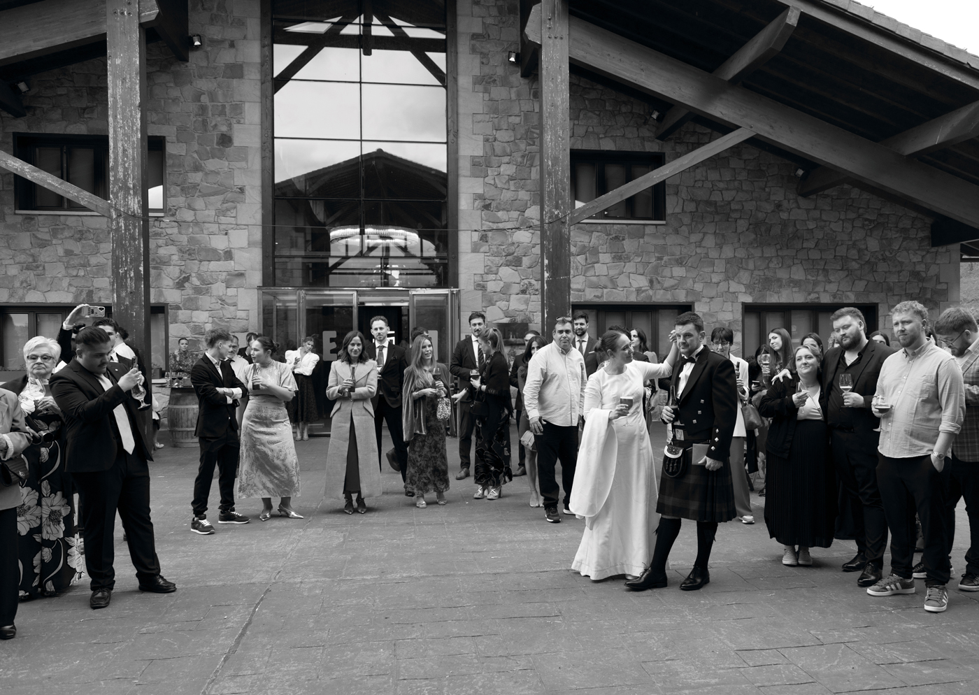 Novios rodeados de invitados celebrando en el exterior durante su boda en Bizkaia, fotografía documental en blanco y negro.
