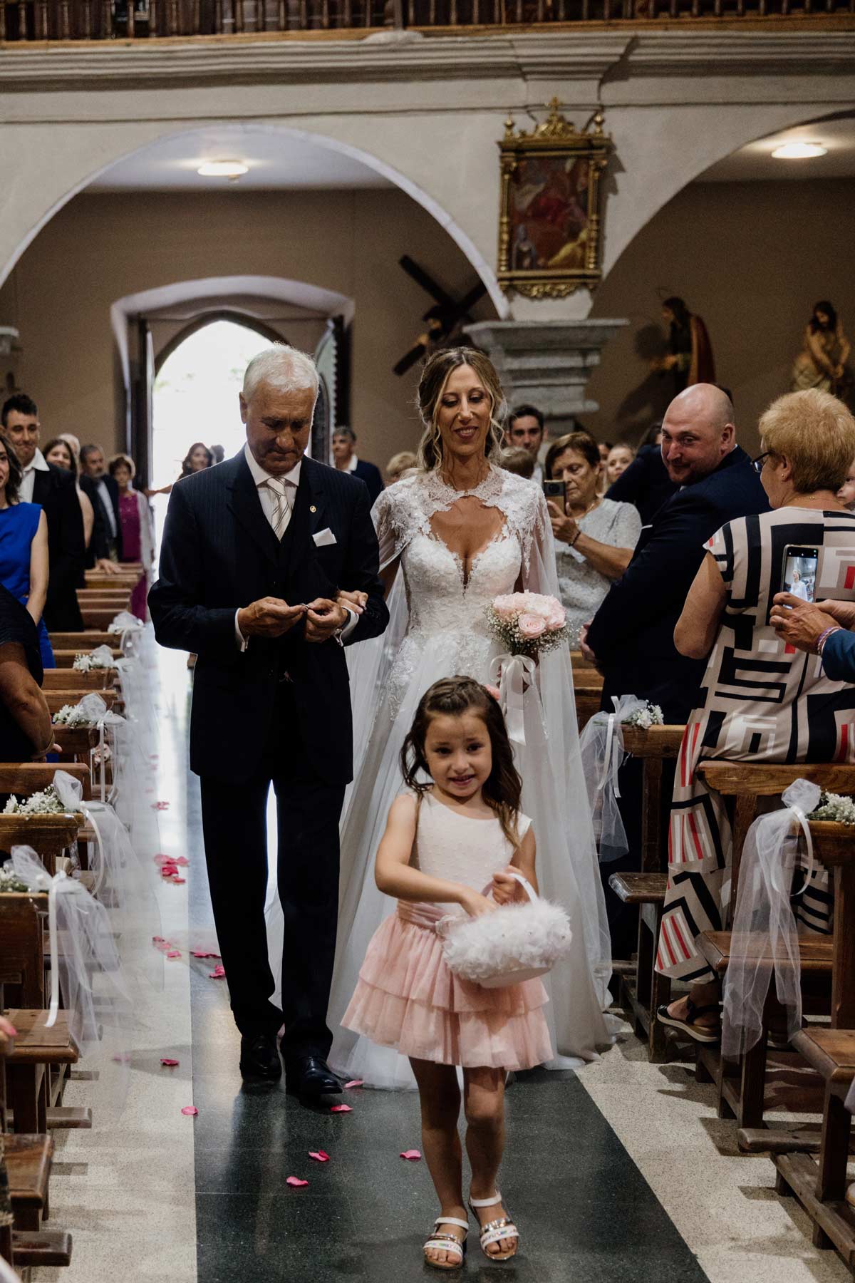 Novia entrando a la iglesia del brazo de su padre durante la ceremonia, acompañada por una niña de arras - fotografía de boda en Bilbao.