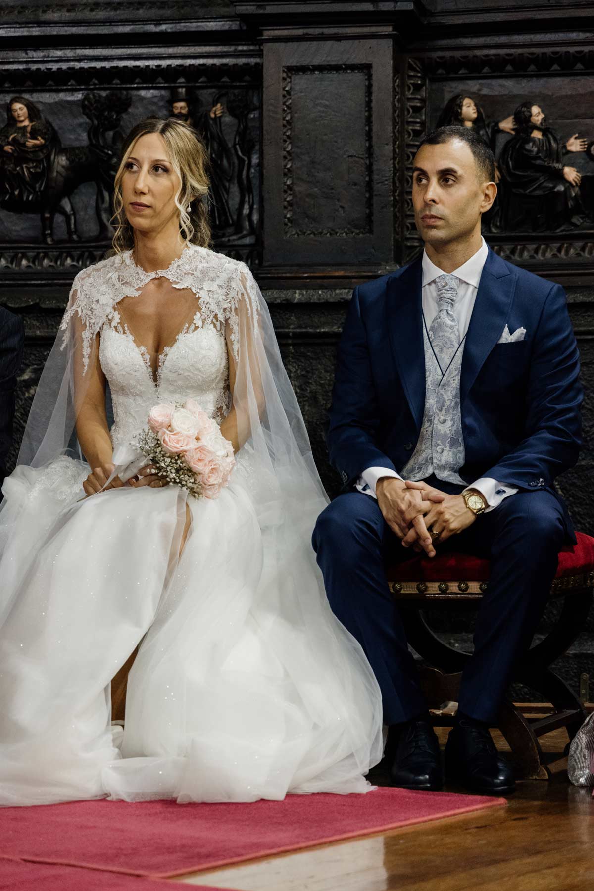 Novios sentados durante la ceremonia religiosa, con la novia sosteniendo su ramo - fotógrafo de bodas en Bilbao.