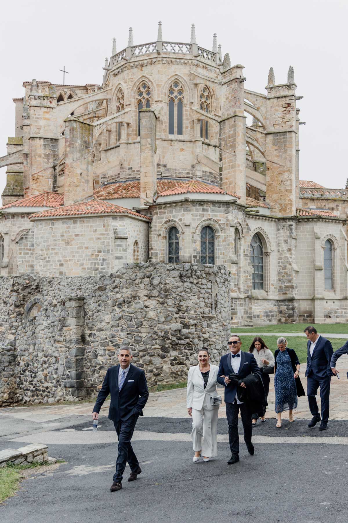 Grupo de invitados y pareja de boda caminando junto a la iglesia de Santa María en Castro Urdiales, Cantabria.