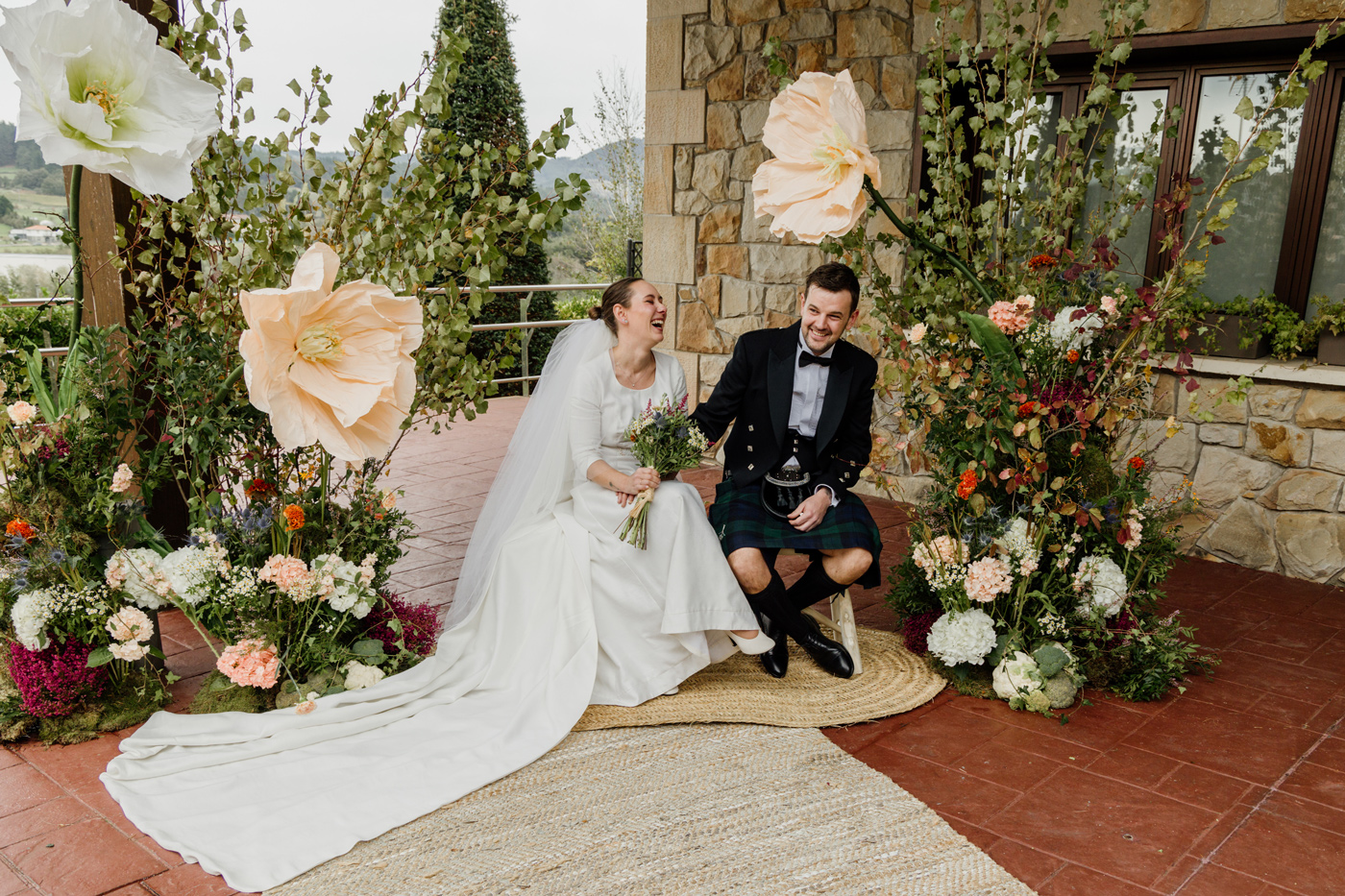Novios riendo juntos entre una decoración floral durante su boda en Bizkaia, fotografía natural de North Producciones.