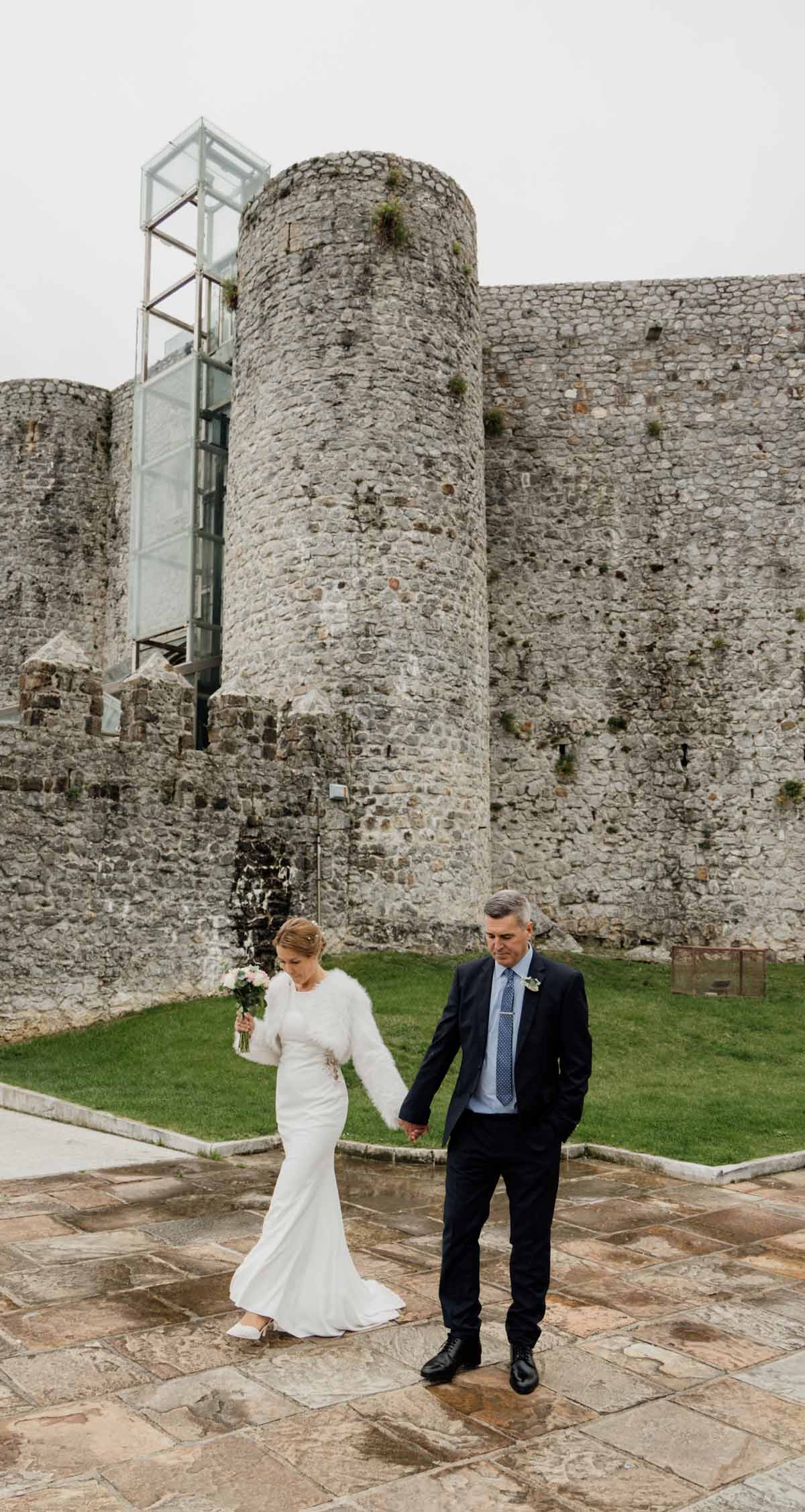 Pareja de recién casados caminando frente a las murallas del castillo-faro De Castro Urdiales durante su boda en Cantabria.
