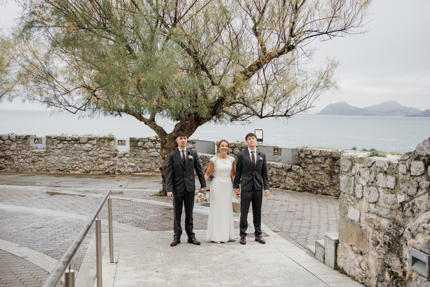 Novia posando junto a dos acompañantes en el paseo marítimo de Castro Urdiales, durante una boda en Cantabria