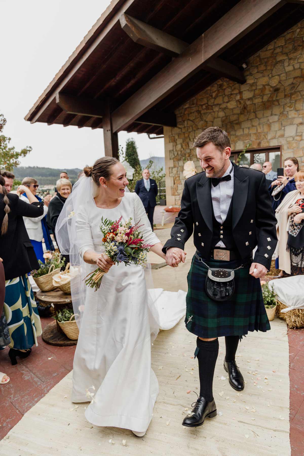 Pareja de recién casados caminando entre aplausos tras la ceremonia, fotografía natural realizada por un fotógrafo de bodas en Bizkaia.