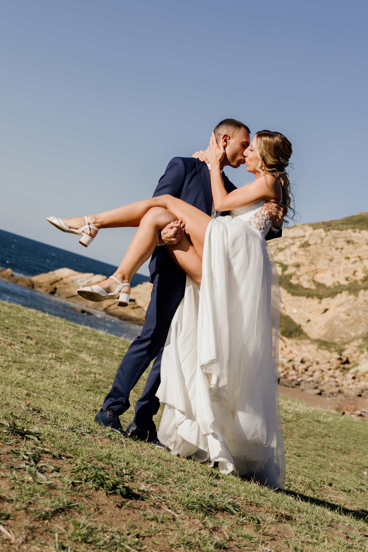 Pareja de novios durante su postboda, con el novio levantando a la novia junto a la costa - Fotógrafo de bodas en Bilbao y Bizkaia.