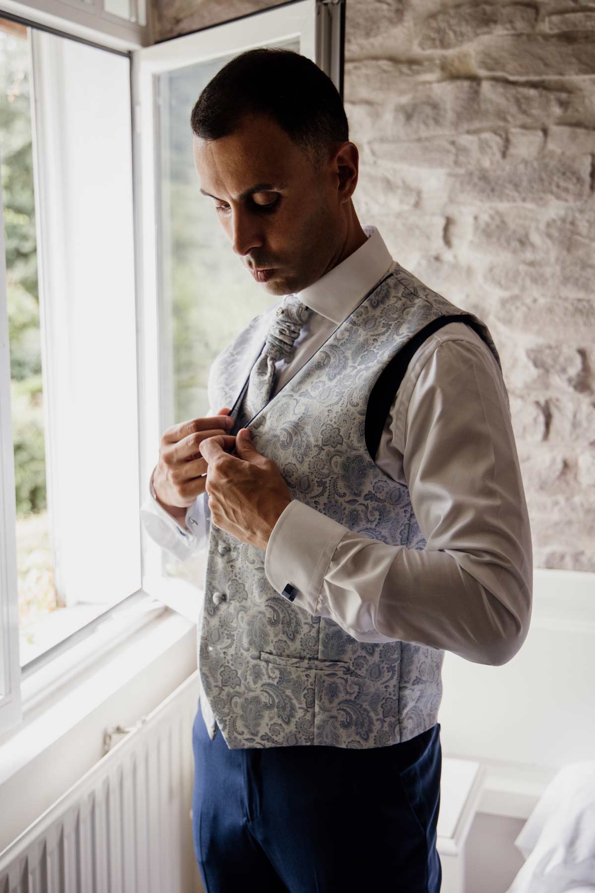 Novio ajustándose la chaqueta junto a una ventana durante los preparativos de boda - fotógrafo de bodas en Bilbao.
