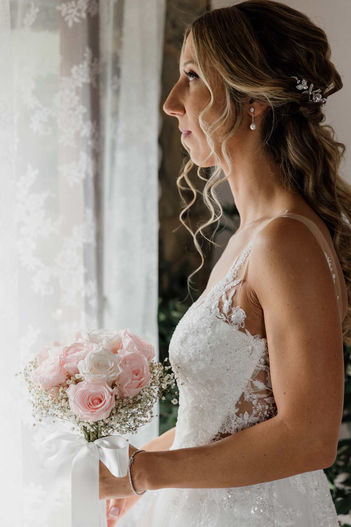 Novia junto a una ventana sosteniendo su ramo durante los preparativos de boda - fotógrafo de bodas en Bilbao.
