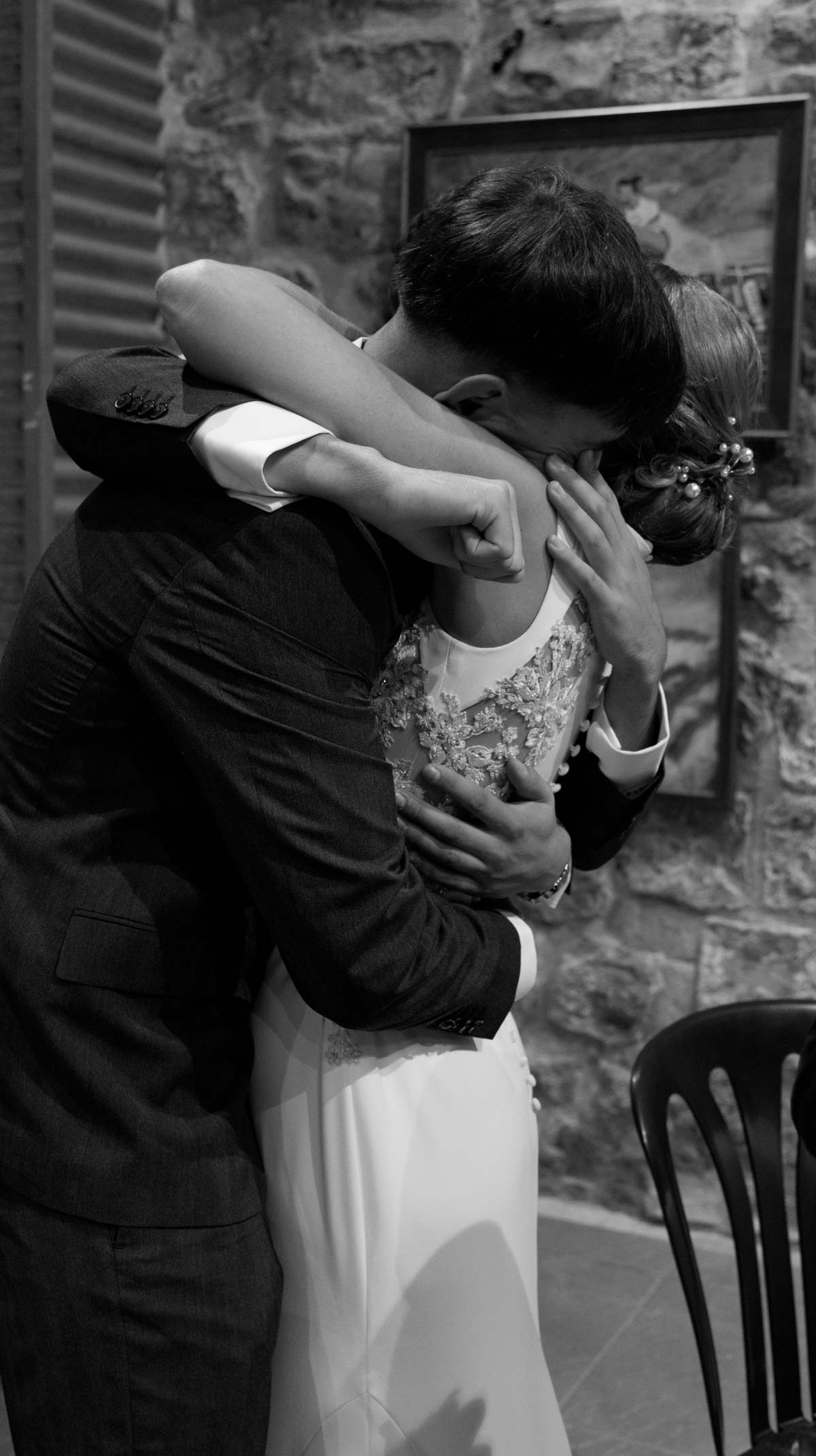 Abrazo emotivo entre amigos durante su boda en un espacio interior de piedra, fotografía en blanco y negro realizada por fotógrafo de bodas en Cantabria.