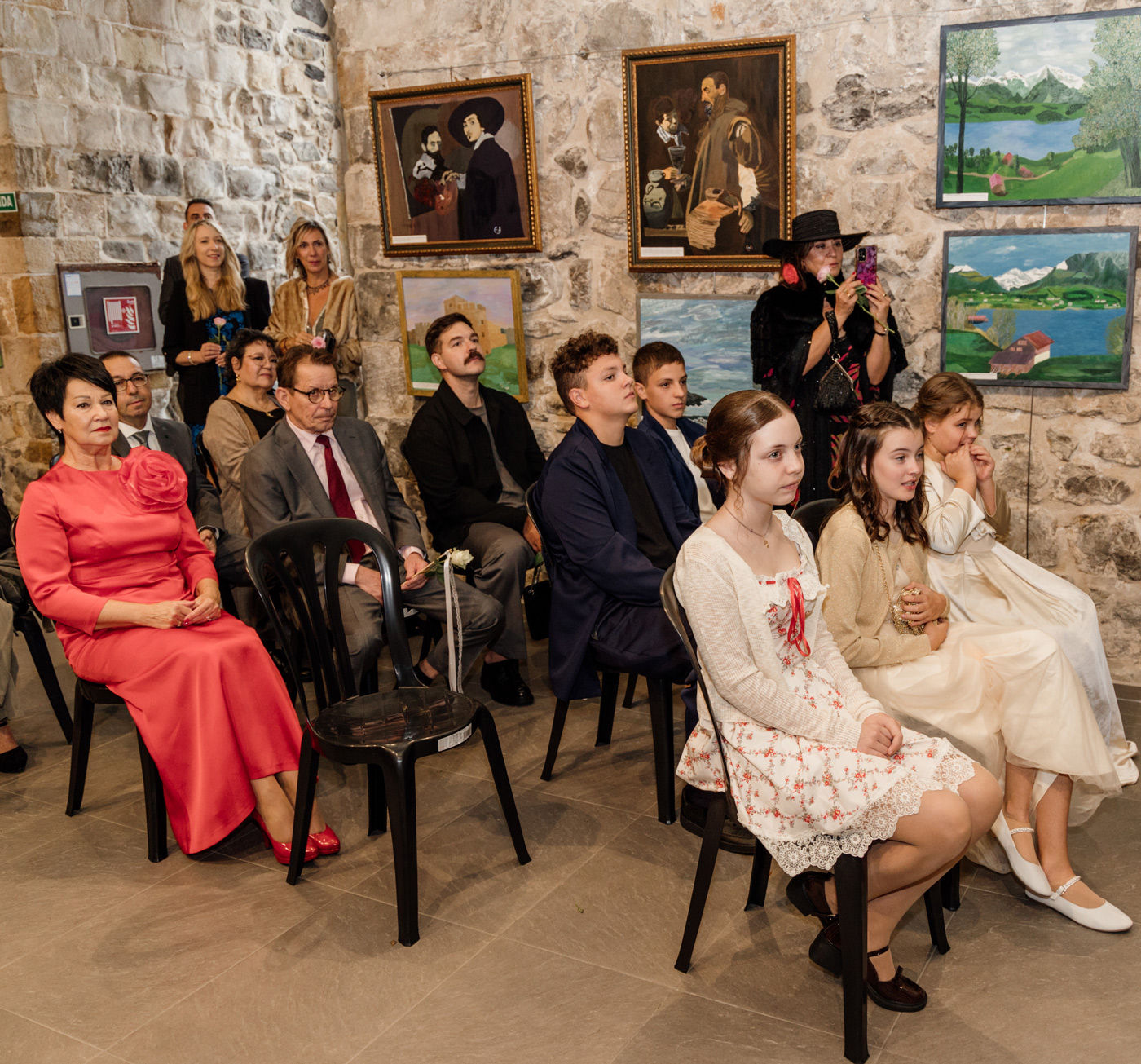 Invitados sentados durante una ceremonia de boda en interior, rodeados de cuadros y paredes de piedra, fotografía de boda en Cantabria