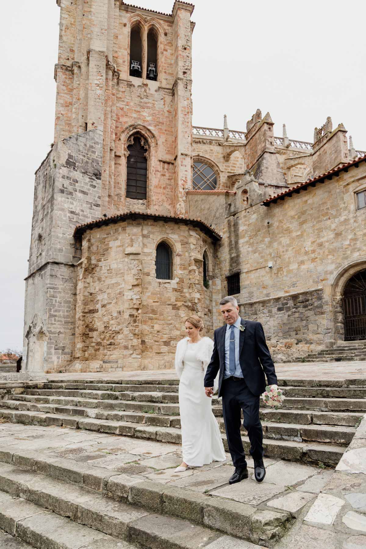 Pareja de recién casados caminando por las escaleras de la iglesia de Santa Maria de la Asunción en Castro Urdiales, fotografía de boda en Cantabria