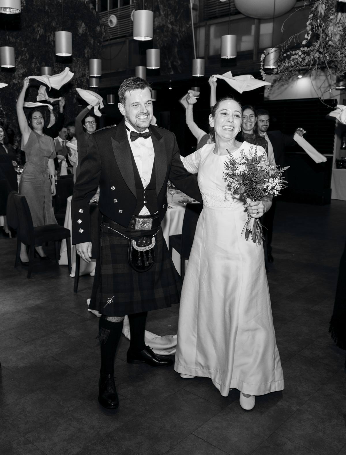 Entrada de los recién casados al banquete mientras los invitados celebran, fotografía documental en blanco y negro realizada por un fotógrafo de bodas en Bizkaia.