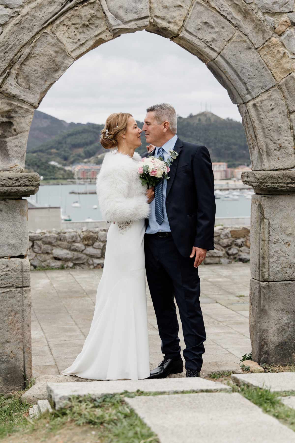 Pareja de recién casados abrazandose bajo un arco de piedra con vistas al mar en Castro Urdiales, fotografía de boda realizada por fotógrafo de bodas en Cantabria.