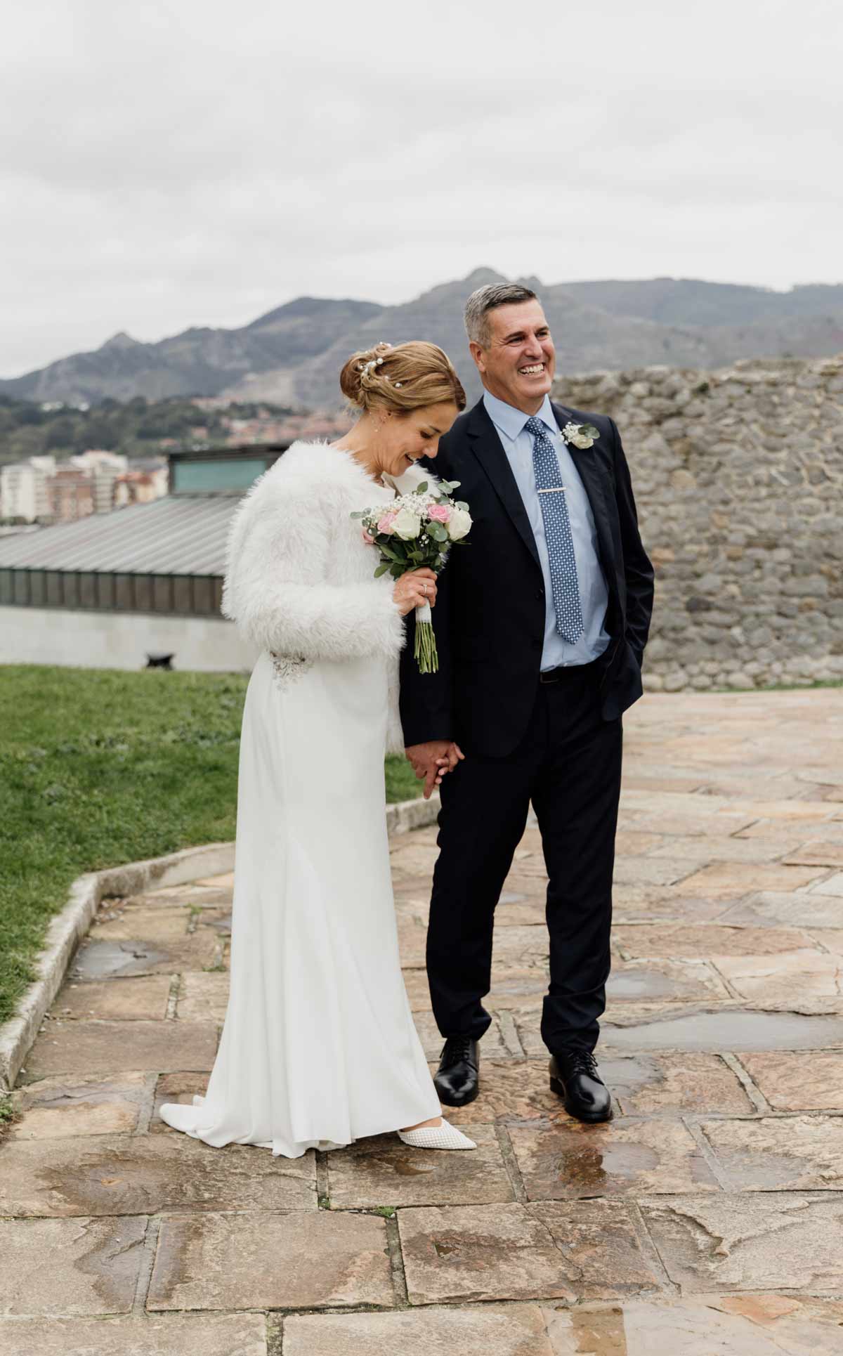Pareja de recién casados caminando de la mano y sonriendo tras la ceremonia en Castro Urdiales, fotografía de boda realizada por fotógrafo de bodas en Cantabria.