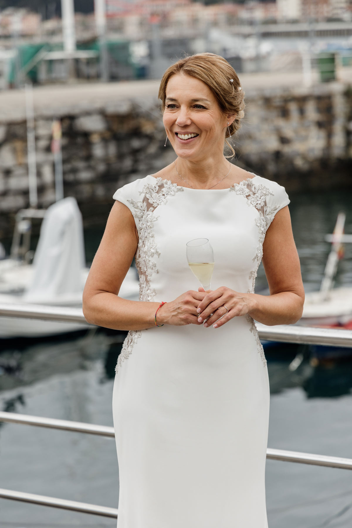 Novia sonriente con copa de champán posando junto al puerto, fotografía de boda realizada por fotógrafo de bodas en Cantabria