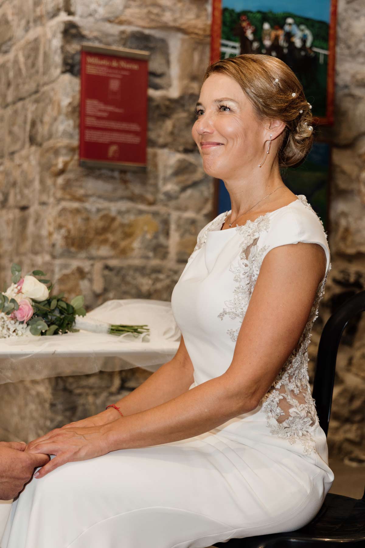 Novia sentada y sonriente durante la ceremonia en un espacio interior de piedra en Cantabria.
