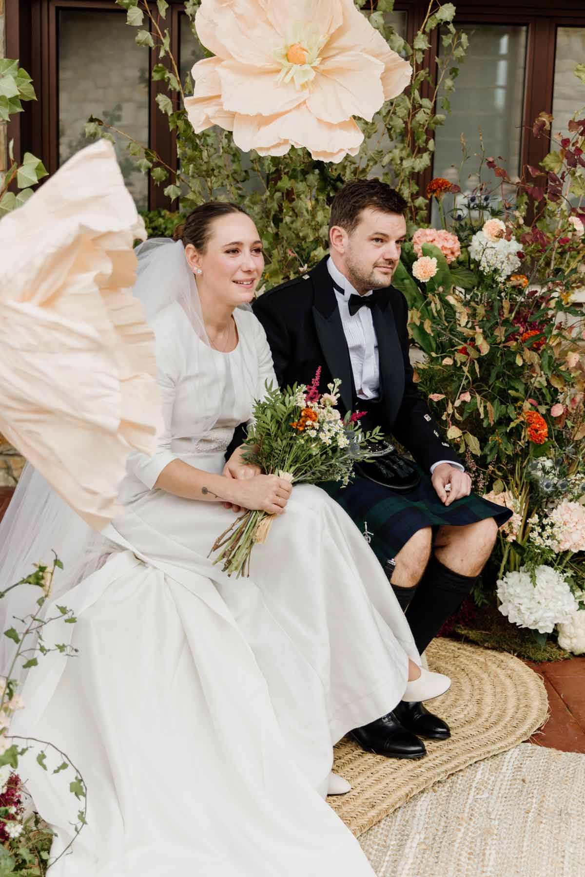 Pareja de recién casados sentada durante la ceremonia entre flores y decoración natural, fotografía de boda realizada por un fotógrafo de bodas en Bizkaia.