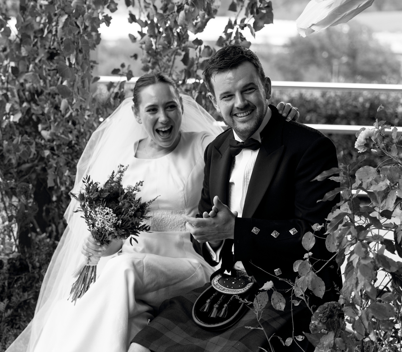 Pareja de recién casados riendo y celebrando al aire libre entre vegetación, fotografía en blanco y negro realizada por un fotógrafo de bodas en Bizkaia.