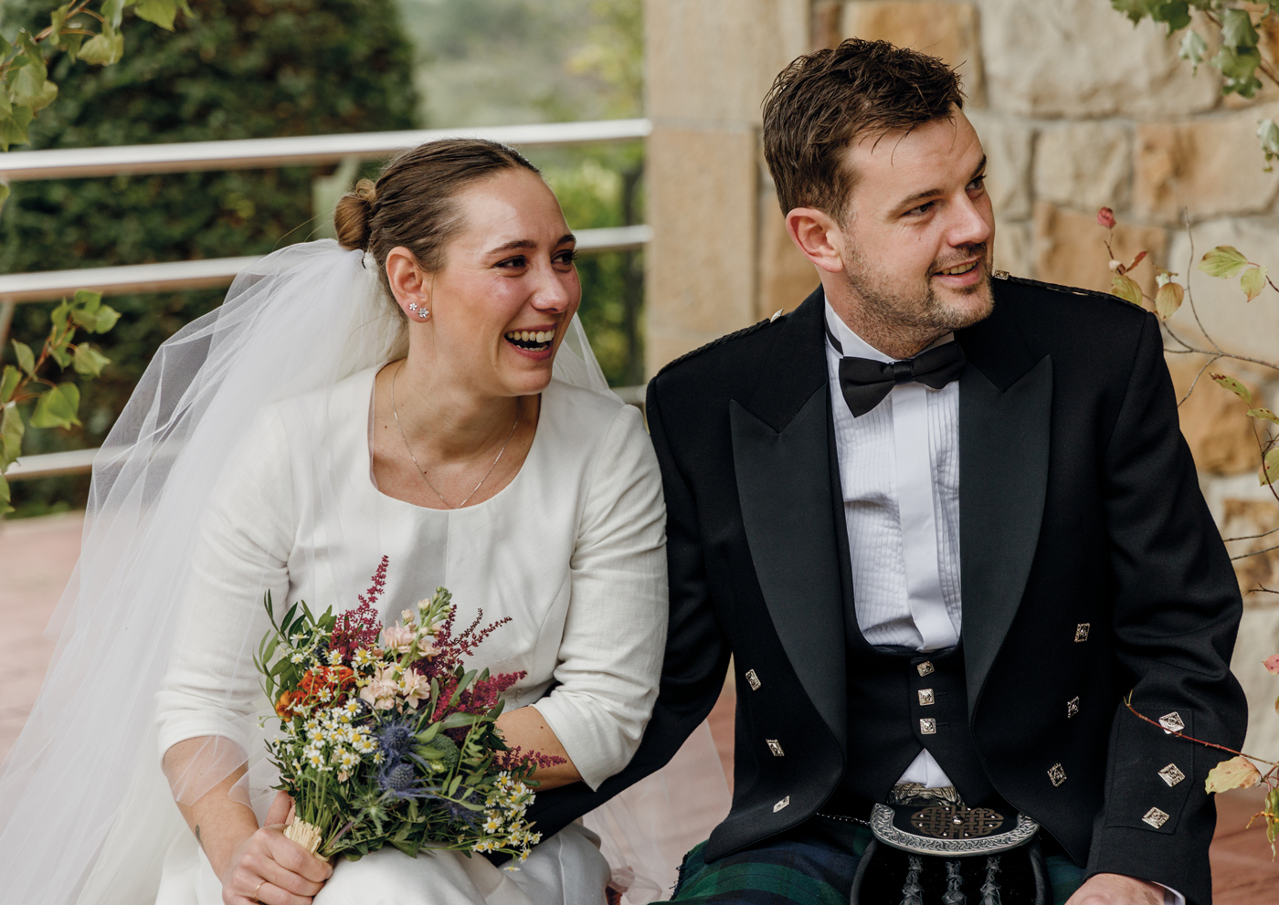 Pareja de recién casados sentada al aire libre y sonriendo con naturalidad, fotografia de boda realizada por un fotógrafo de bodas en Bizkaia.